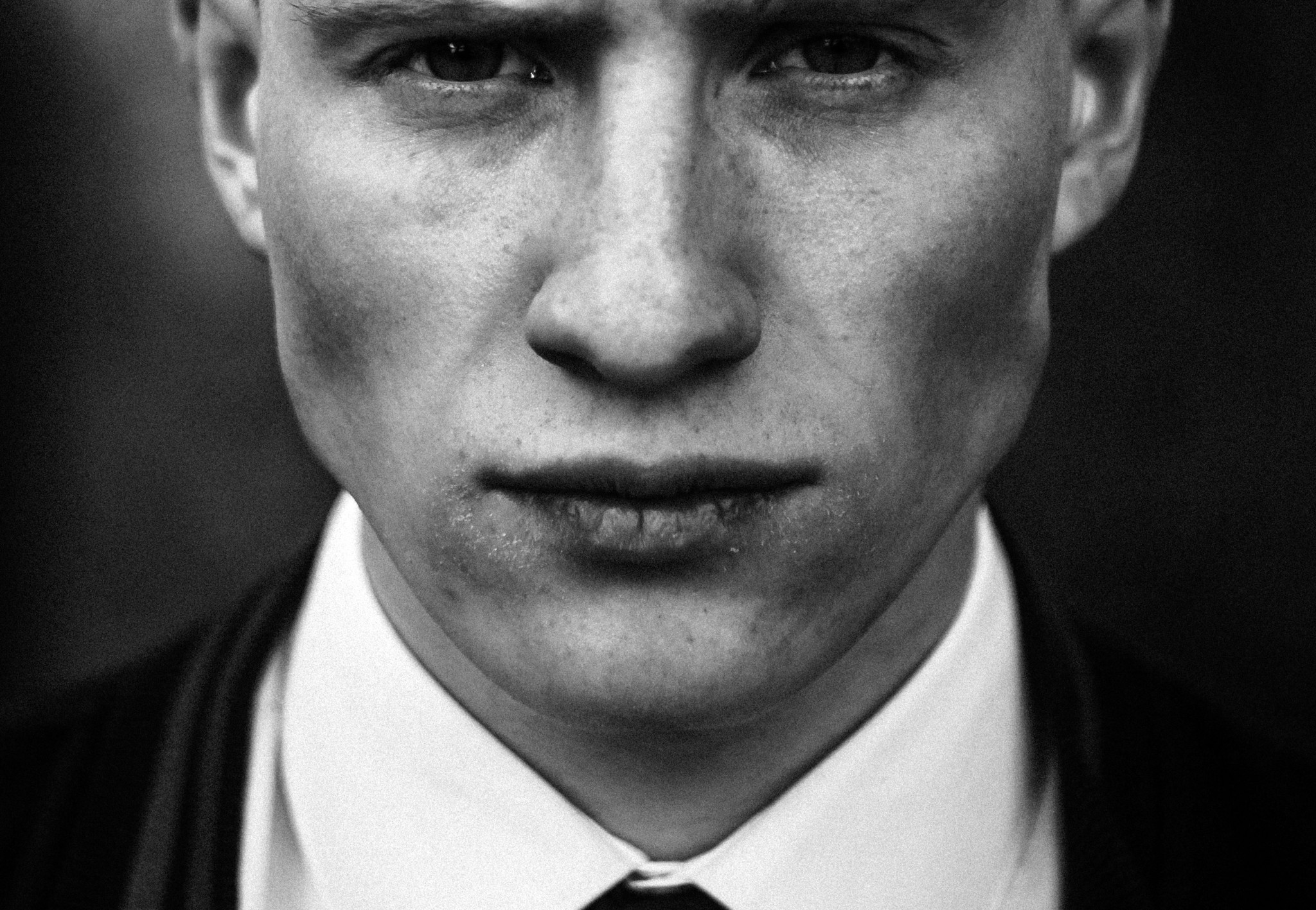 Portrait en noir et blanc d’un jeune homme au regard intense, vêtu d’un costume et d’une cravate.