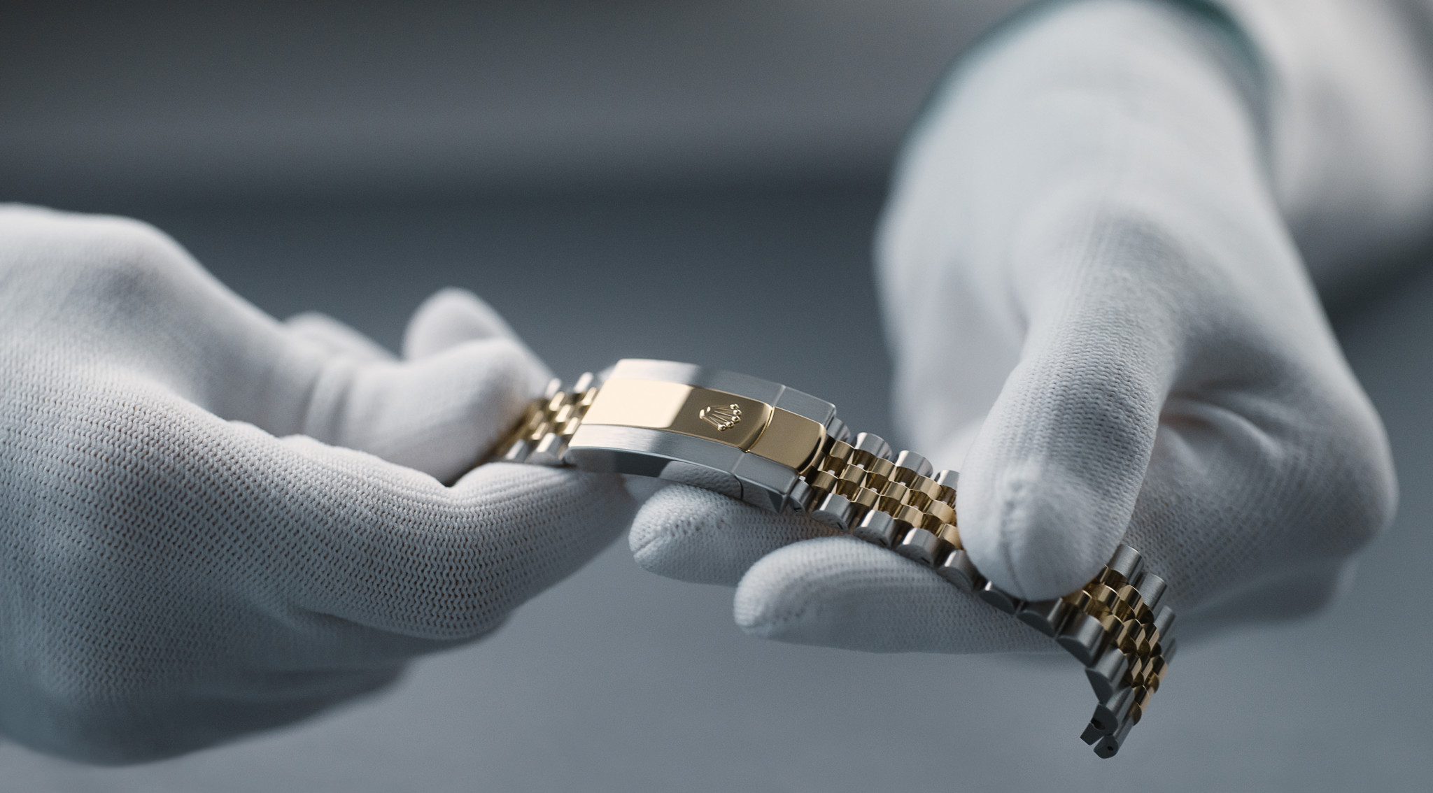 Gants blancs tenant un bracelet de montre en métal bicolore avec un fermoir doré.