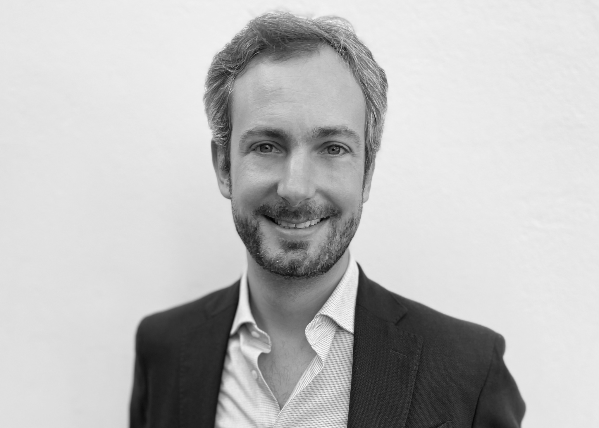 Portrait en noir et blanc d’un homme souriant en veste sombre sur fond clair