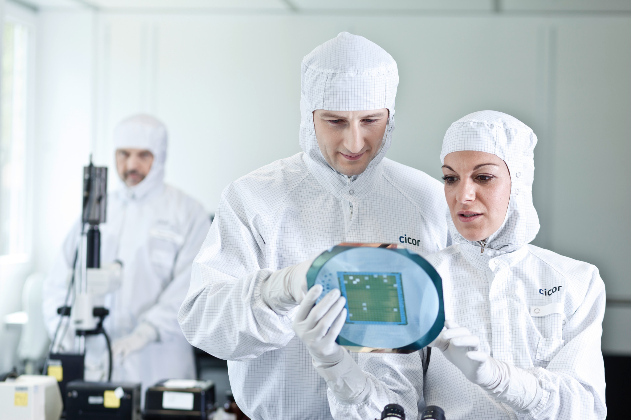 Deux scientifiques en combinaisons de laboratoire inspectent une plaquette de semi-conducteurs dans un environnement stérile.