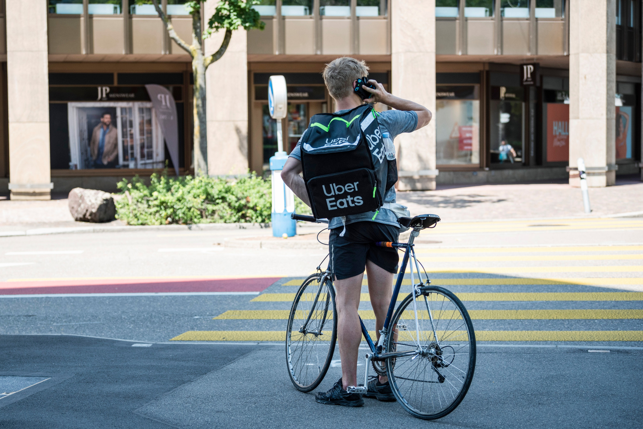 Livreur Uber Eats à vélo avec sac à dos noir de livraison, attendant à un carrefour de Zurich