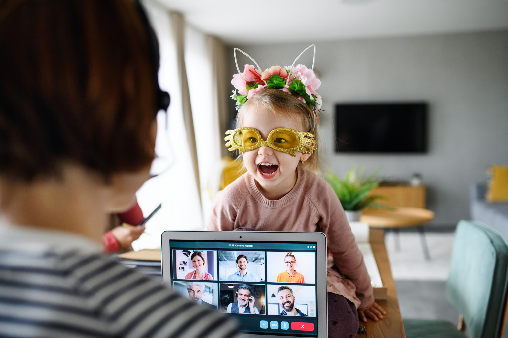 Petite fille souriante avec lunettes dorées et serre-tête fleuri devant un appel vidéo en famille sur tablette à la maison