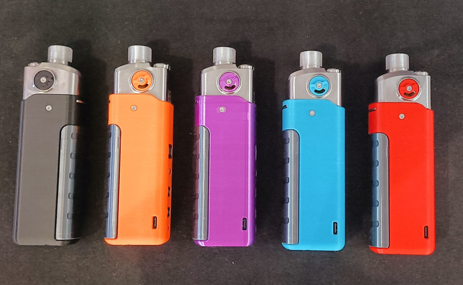 Cinq vaporisateurs de différentes couleurs alignés sur une surface noire : noir, orange, violet, bleu et rouge.