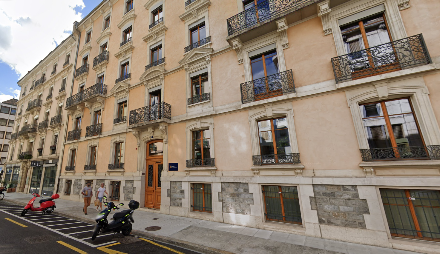 Immeuble haussmannien beige avec balcons en fer forgé à Genève, scooters garés devant sur le trottoir.