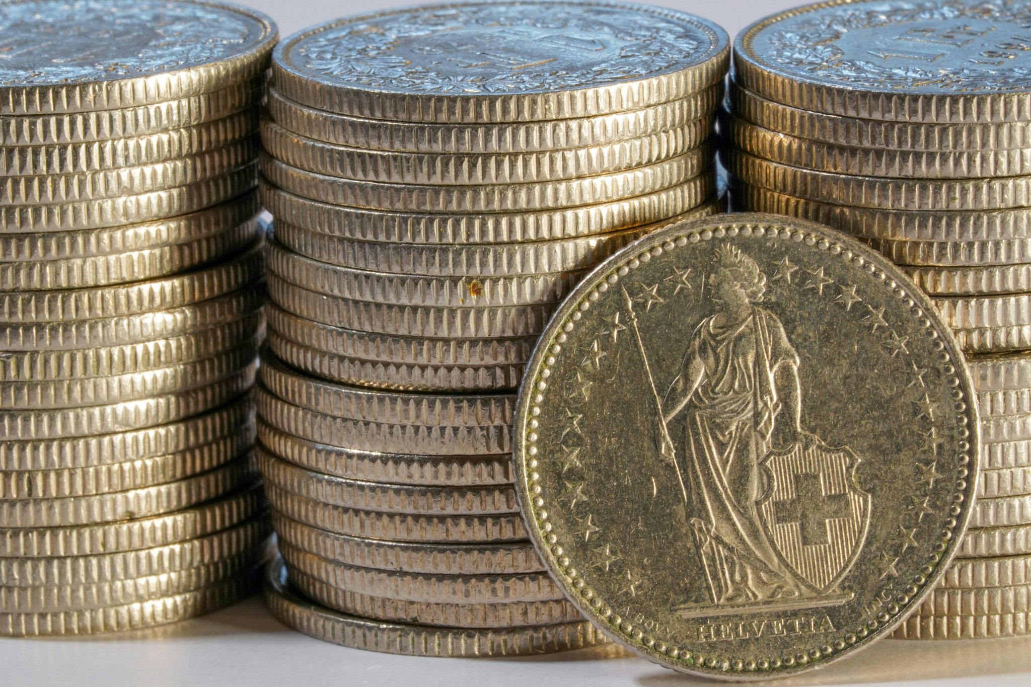 Piles de pièces de francs suisses avec une pièce Helvetia au premier plan, arborant la croix suisse et l’inscription HELVETIA