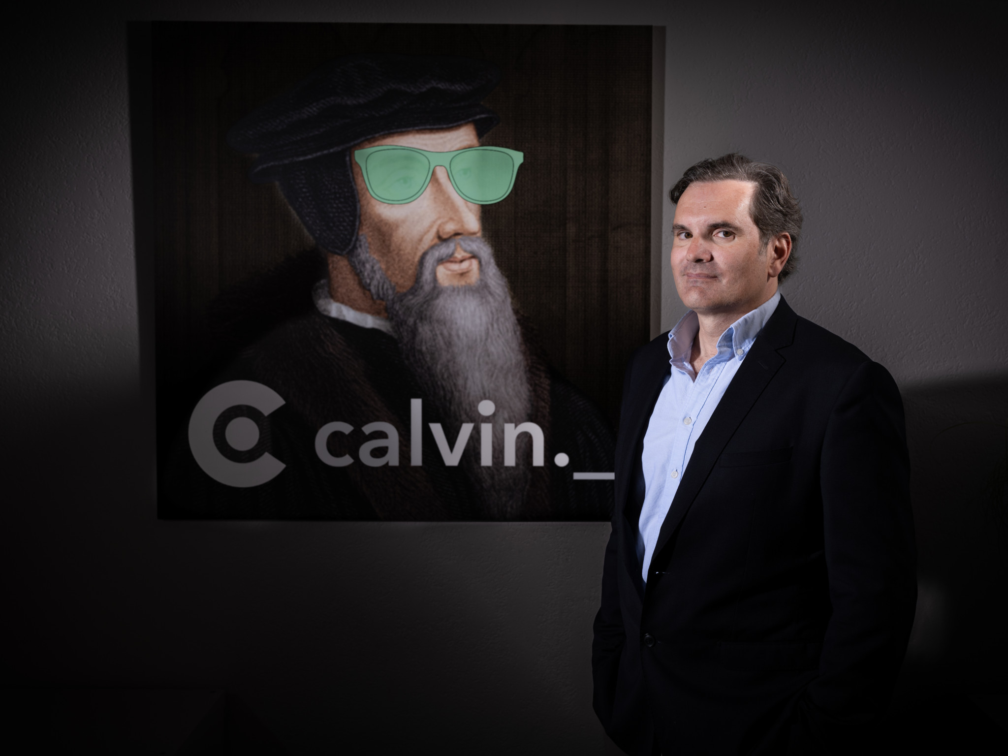 Thomas Le Forestier, actif dans le leasing, devant le logo Calvin.ch avec un portrait revisité de Calvin arborant des lunettes vertes, à Genève.