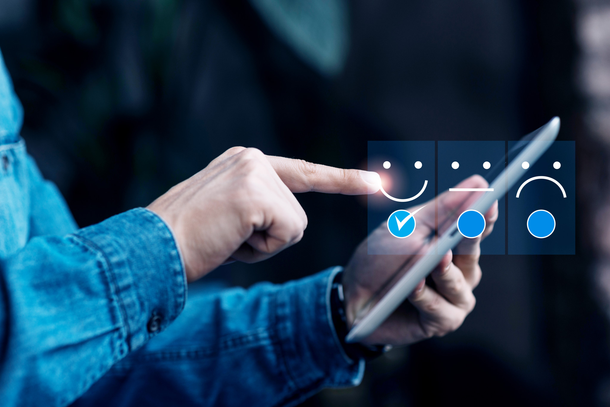 Homme en chemise en jean touchant une tablette avec trois icônes d’émotions : sourire, neutre et triste.
