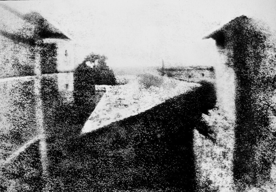 La plus ancienne photographie connue, en noir et blanc granuleuse, montrant des toits et bâtiments vus depuis une fenêtre.