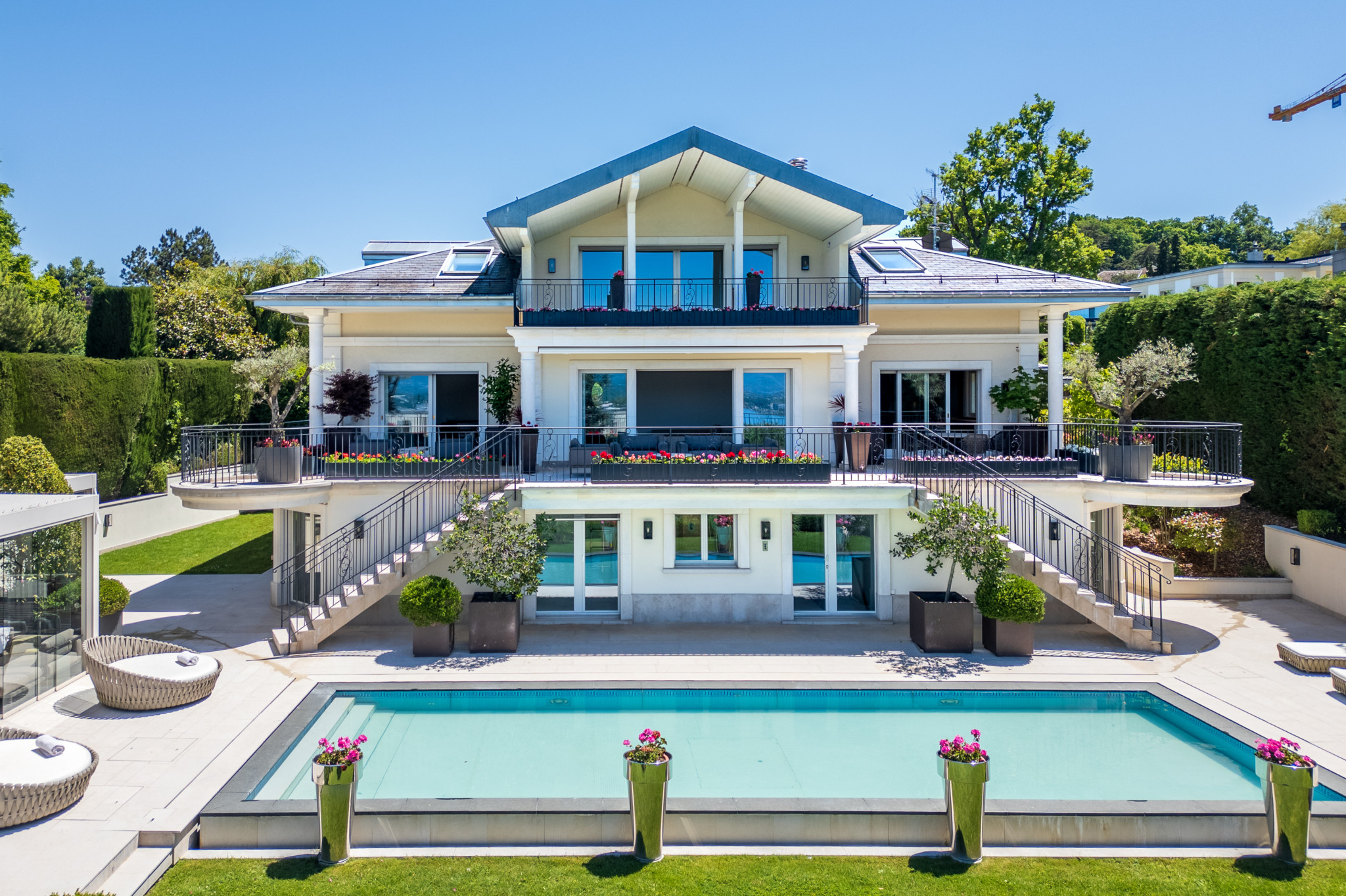 Grande villa blanche moderne avec piscine, entourée de jardins paysagers et terrasse spacieuse.