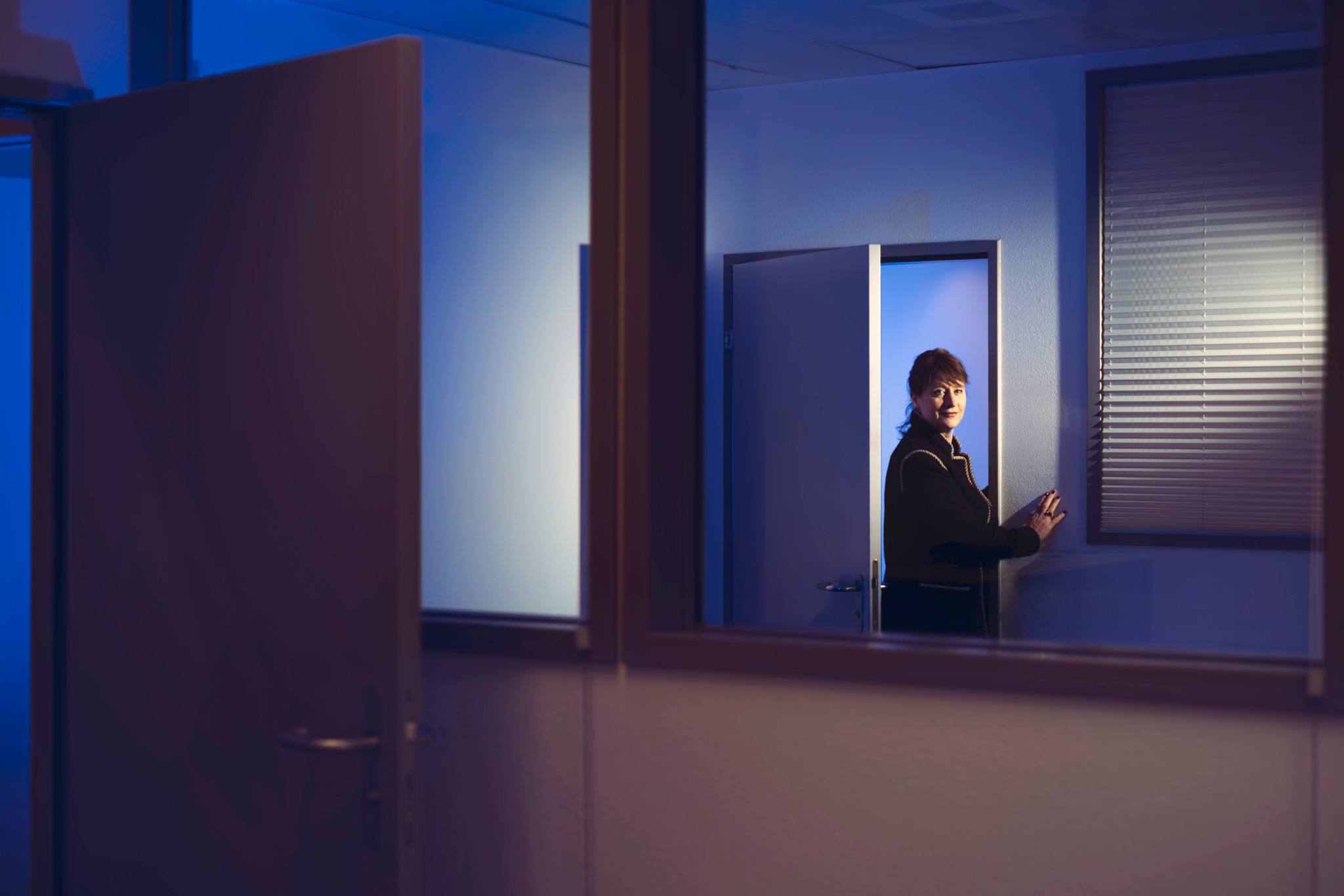 Personne entrant dans une pièce sombre, éclairée par une lumière bleue, tenant un téléphone.