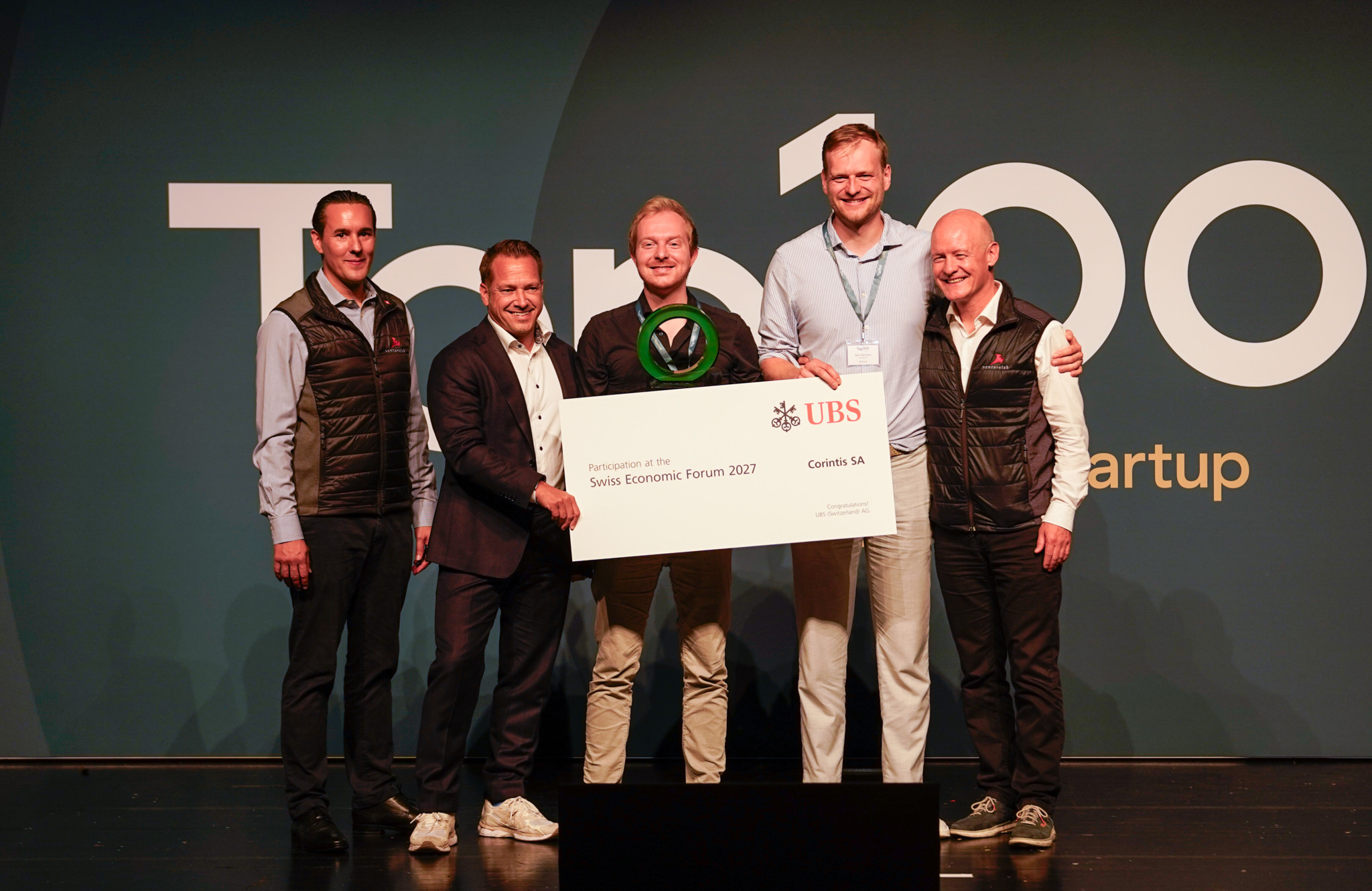 Cinq hommes souriant sur scène tenant un grand chèque UBS lors du Swiss Economic Forum 2027, événement Top 100 Startup.
