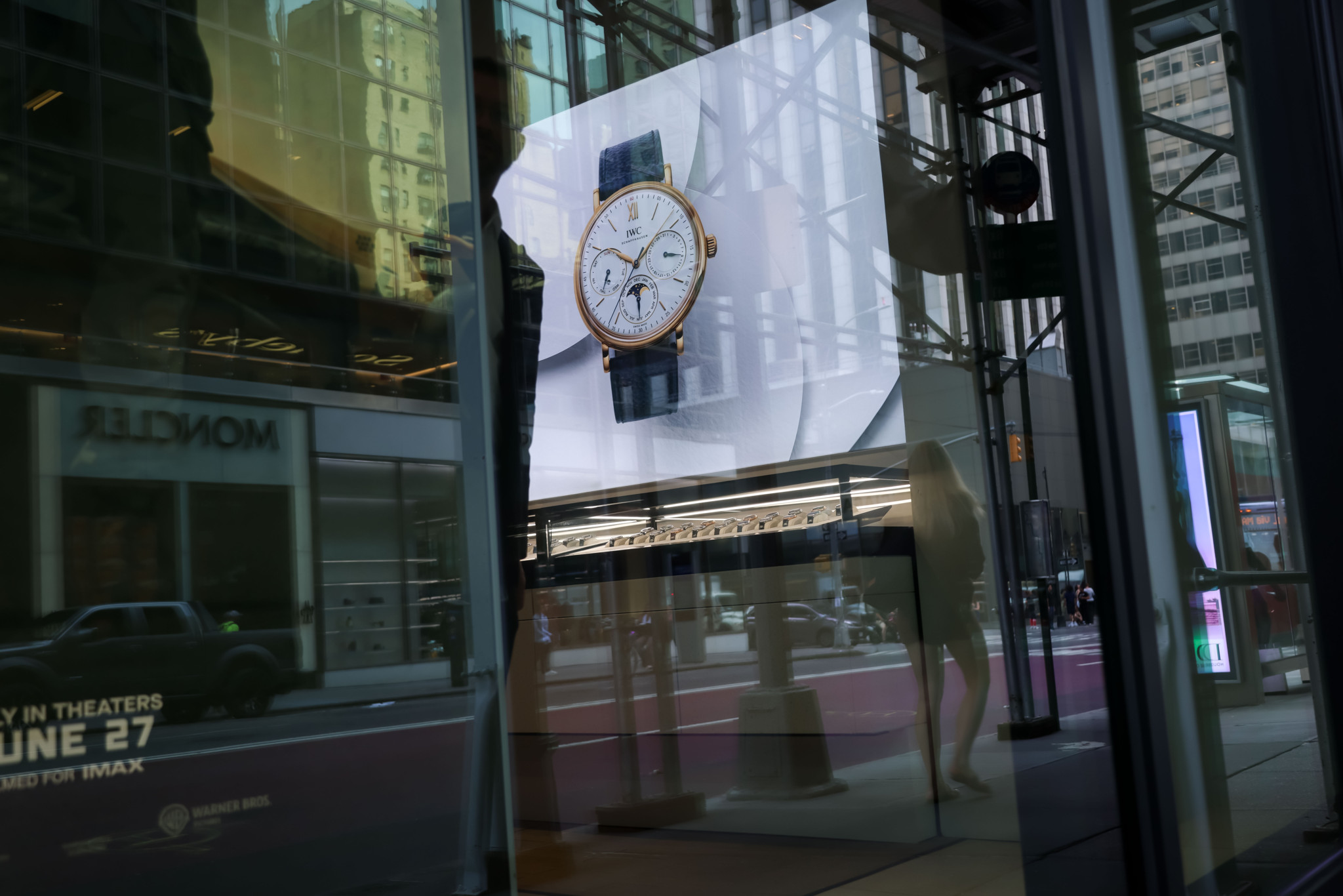 Affichage à l’intérieur d’une boutique IWC à New York, montrant une montre de luxe, avec des passants et des bâtiments en arrière-plan.