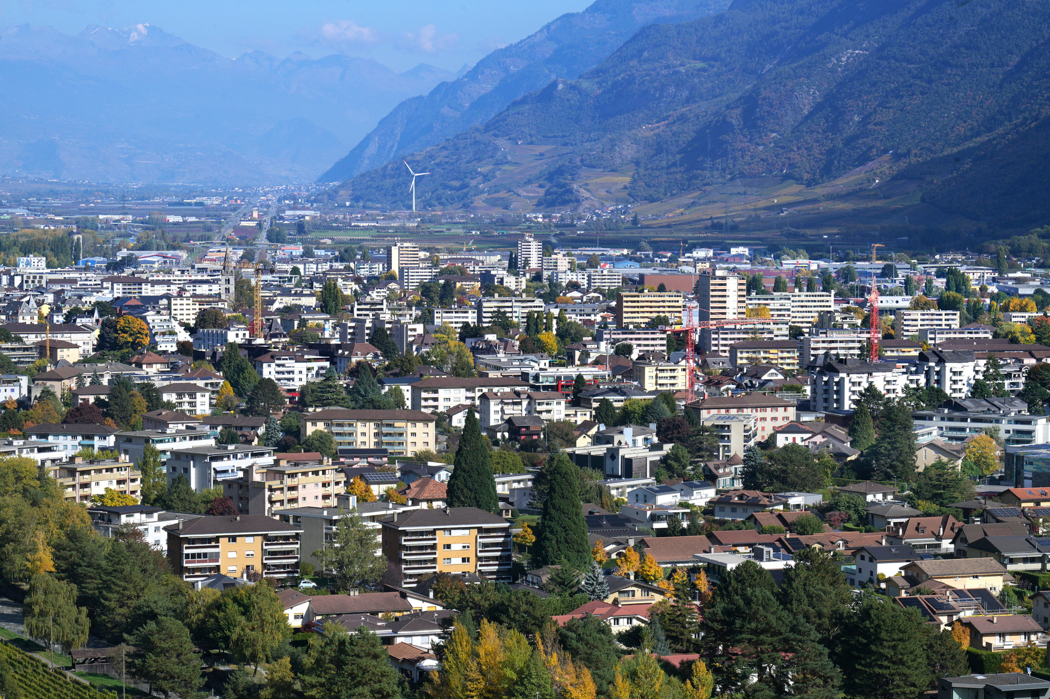 Vue panoramique de la ville de Martigny en Valais, entourée de montagnes alpines et de végétation automnale colorée.