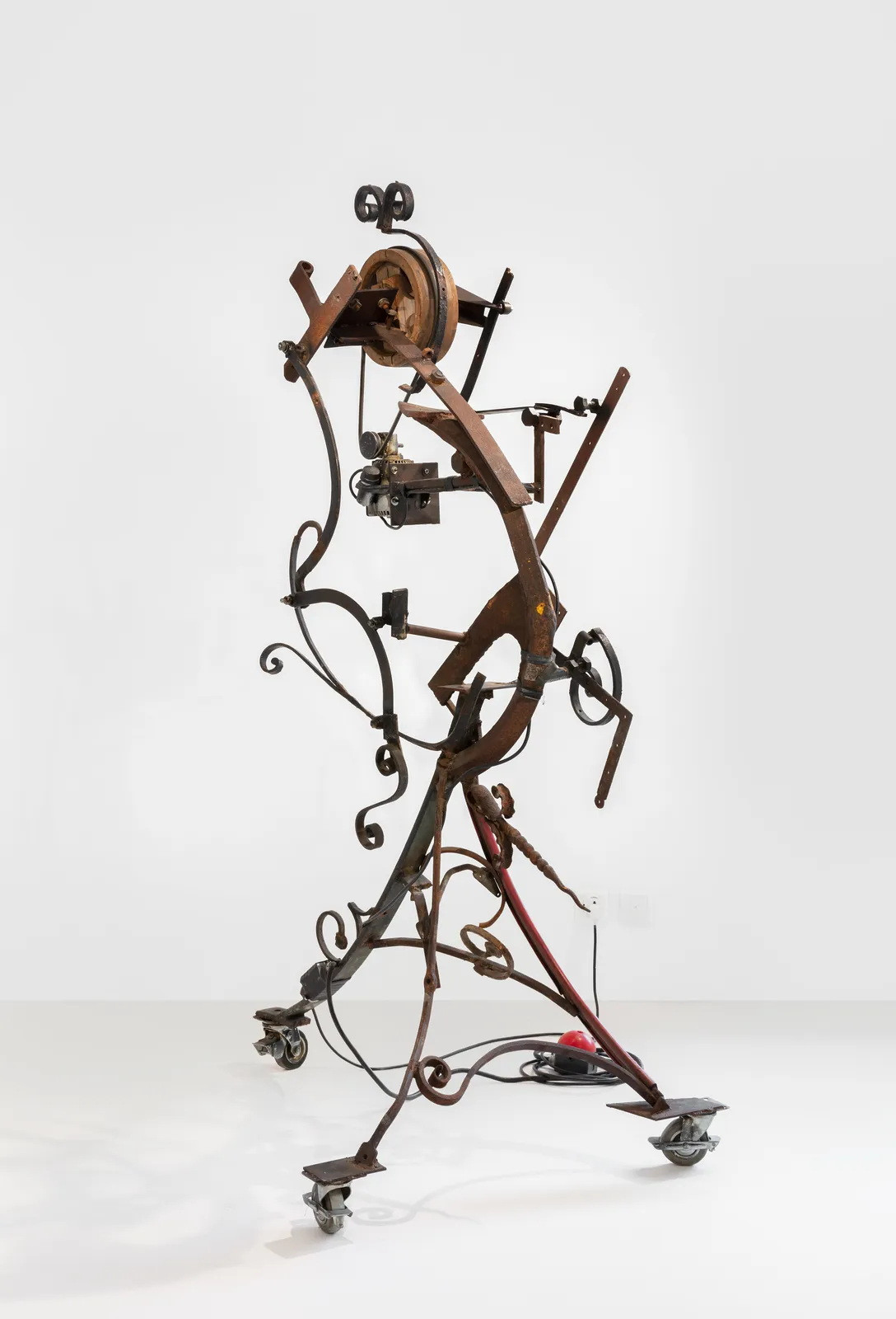 Sculpture abstraite en métal rouillé sur roulettes, assemblage de pièces mécaniques et ferronnerie formant une silhouette humanoïde.
