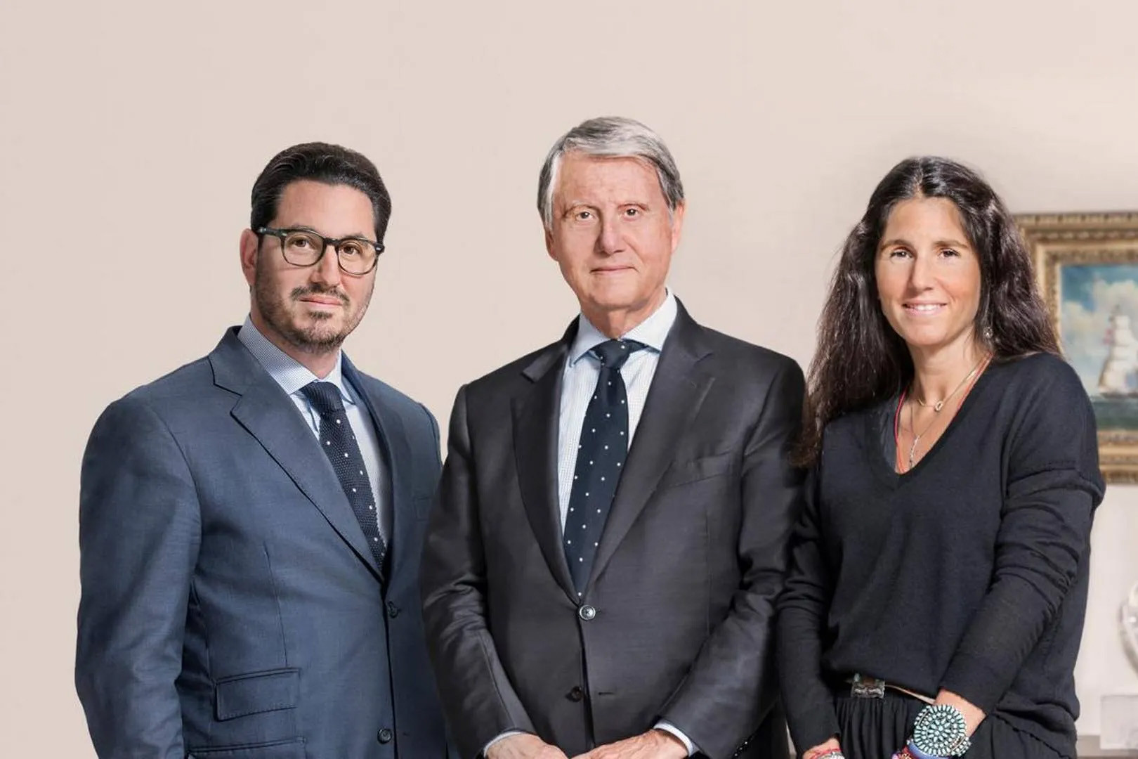 Trois personnes en tenue professionnelle posant ensemble : deux hommes en costumes sombres et une femme en tenue noire, devant un fond neutre clair.