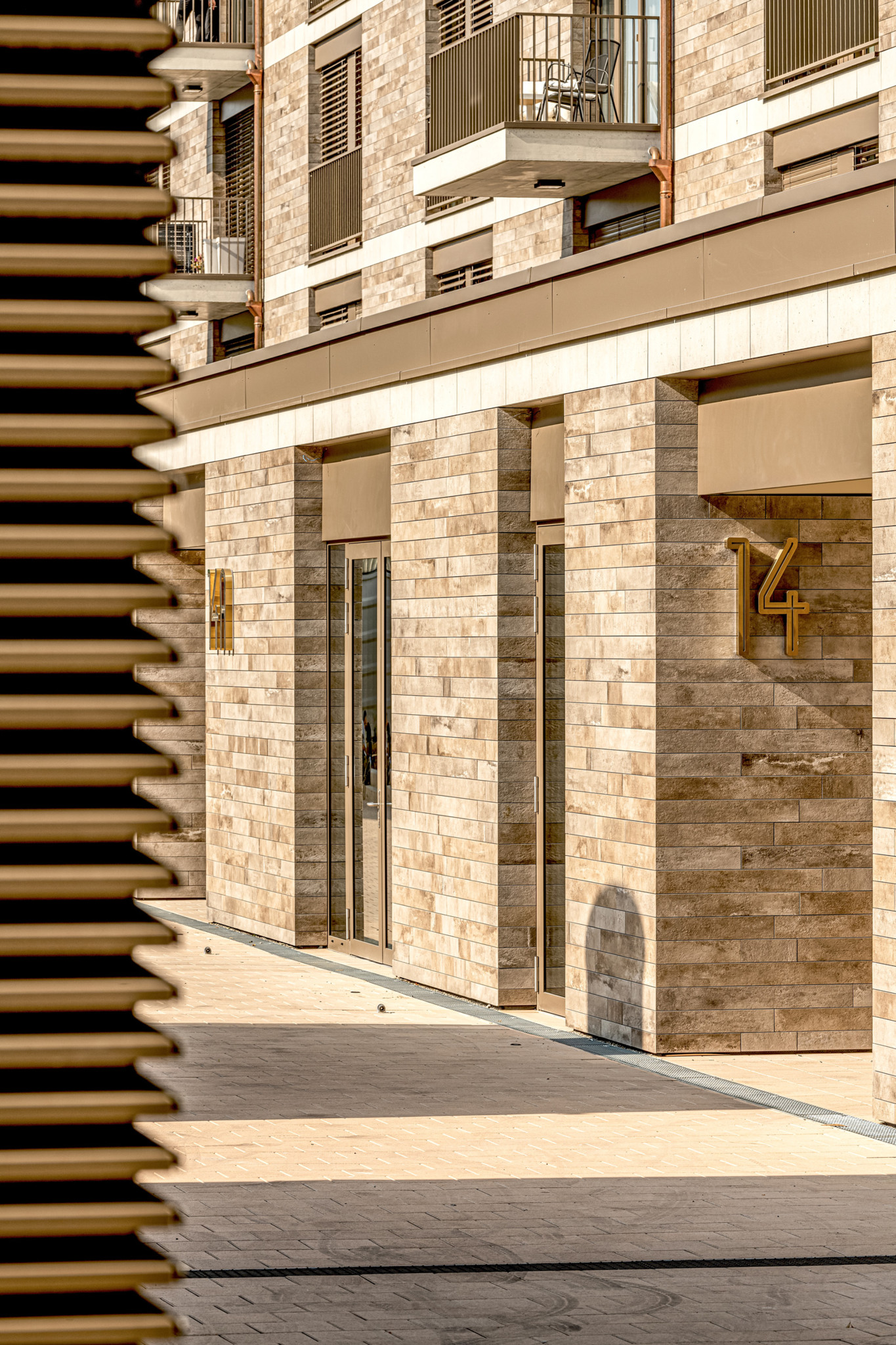 Vue en contre-plongée d’un patio moderne avec des murs blancs perforés et des fenêtres en bois encadrant un ciel lumineux.