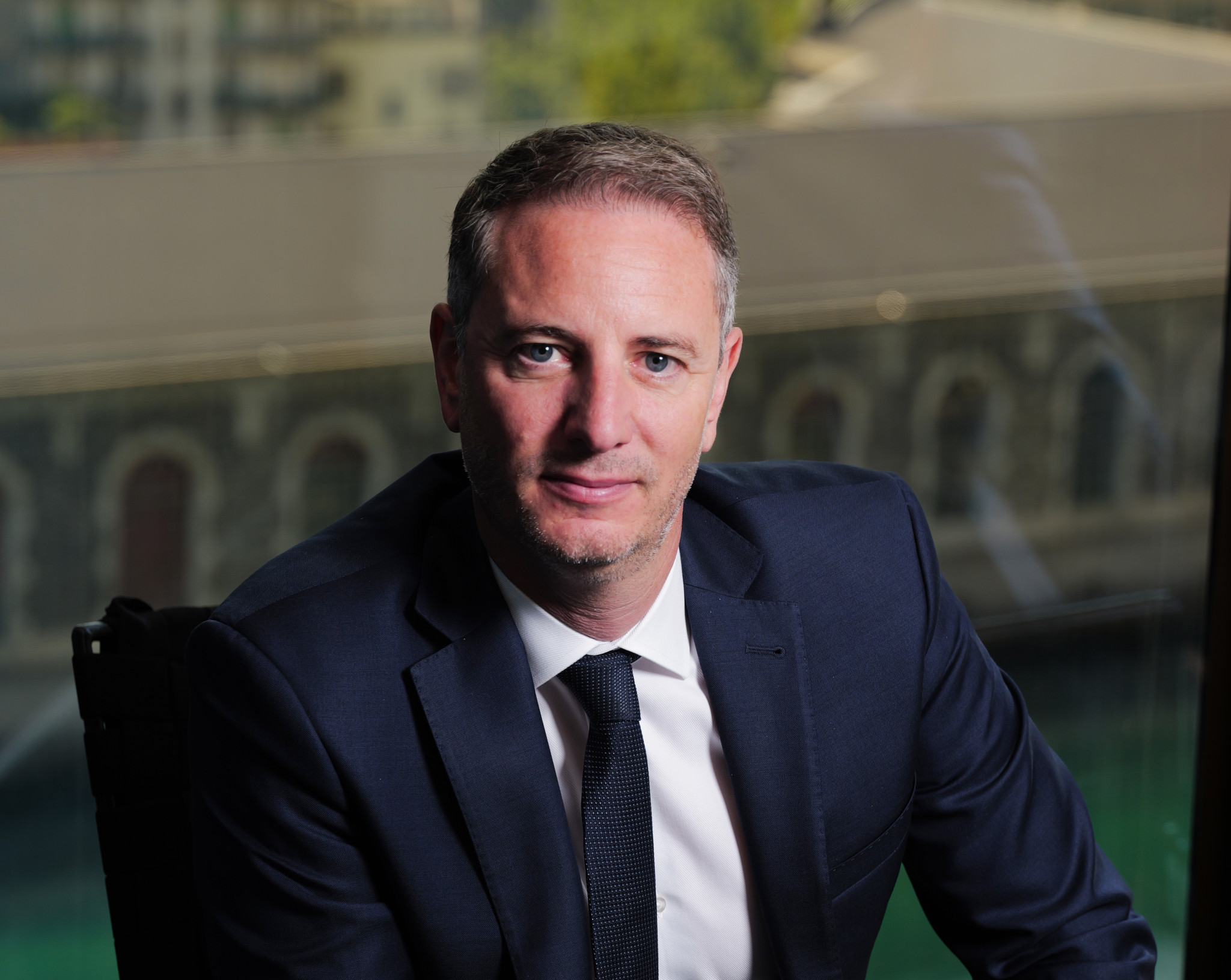 Arnaud Bürgin, directeur de la FER, en costume sombre et cravate, posant devant une fenêtre avec vue sur Genève.