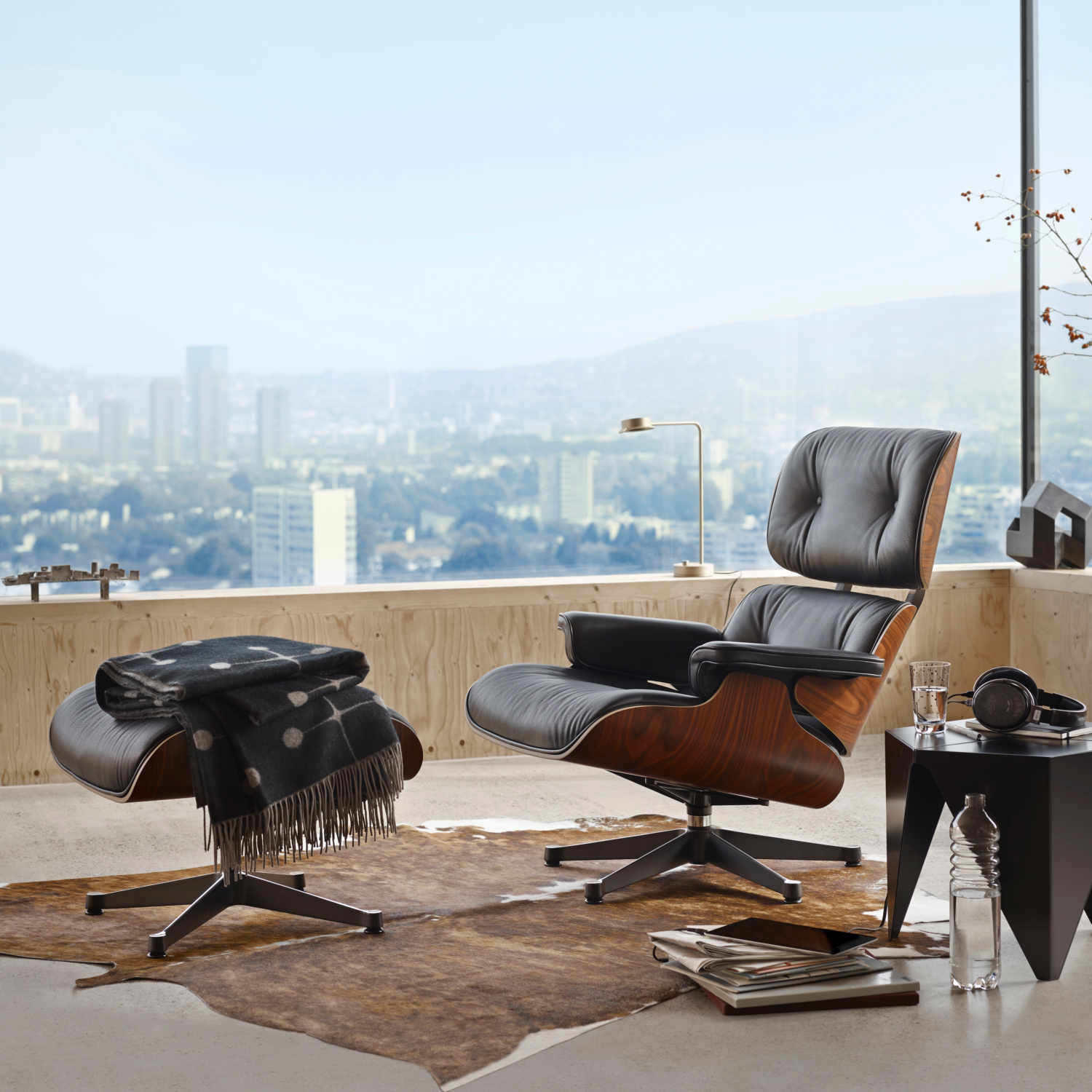 Fauteuil en cuir noir et bois avec repose-pieds dans un salon moderne, avec vue panoramique sur une ville.