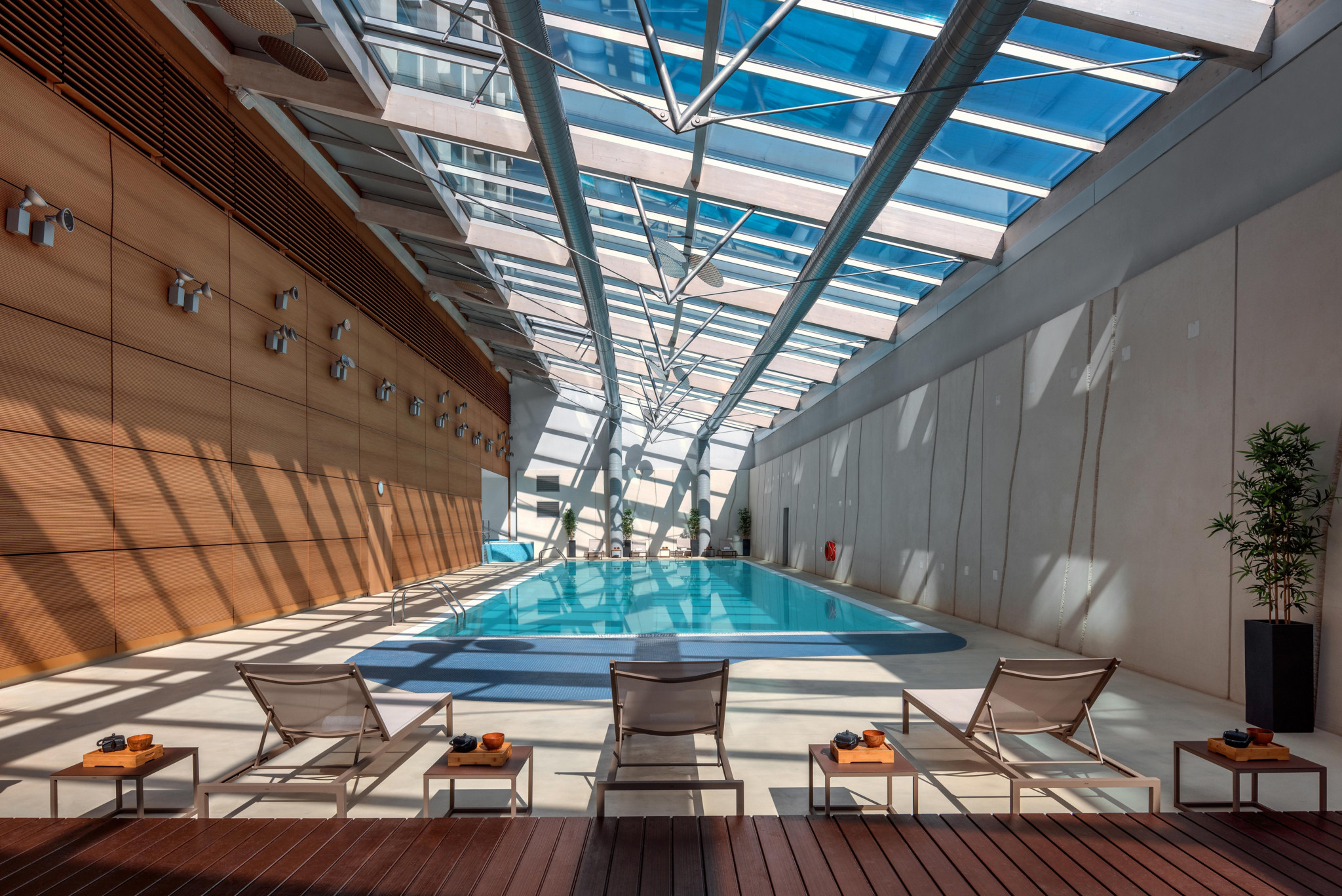Piscine intérieure luxueuse avec verrière, chaises longues sur plancher en bois et murs en bois chaleureux dans un hôtel haut de gamme