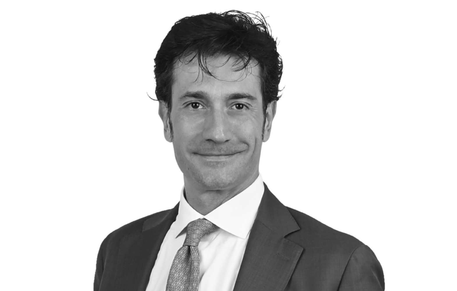 Portrait en noir et blanc d’un homme en costume et cravate, souriant face à l’objectif sur fond blanc.