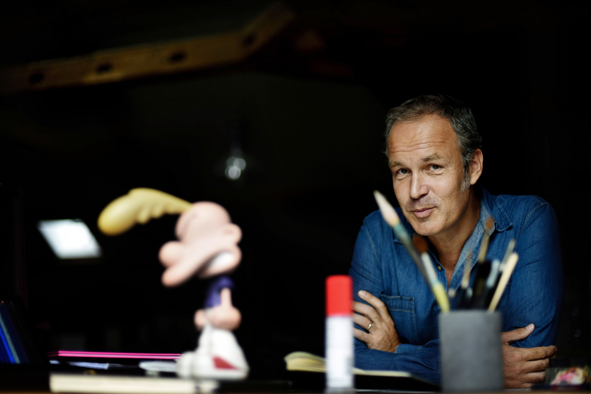 Zep dans son atelier à Genève, entouré de pinceaux et de matériel artistique, avec une figurine de Titeuf au premier plan, avant la sortie d’un nouvel album de Titeuf en 2017.