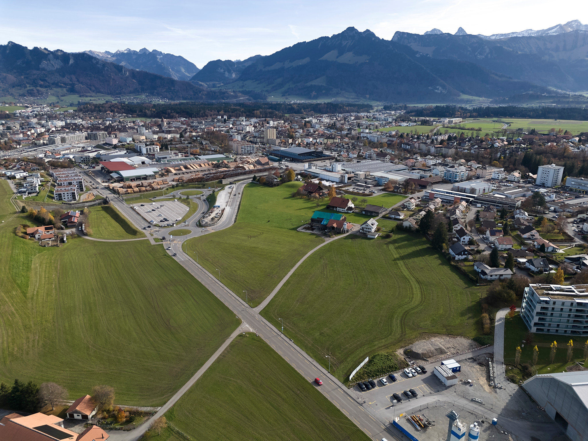 Vue aérienne des champs à l’ouest de Bulle destinés au futur quartier La Pâla, avec la ville et les Préalpes fribourgeoises en arrière-plan.