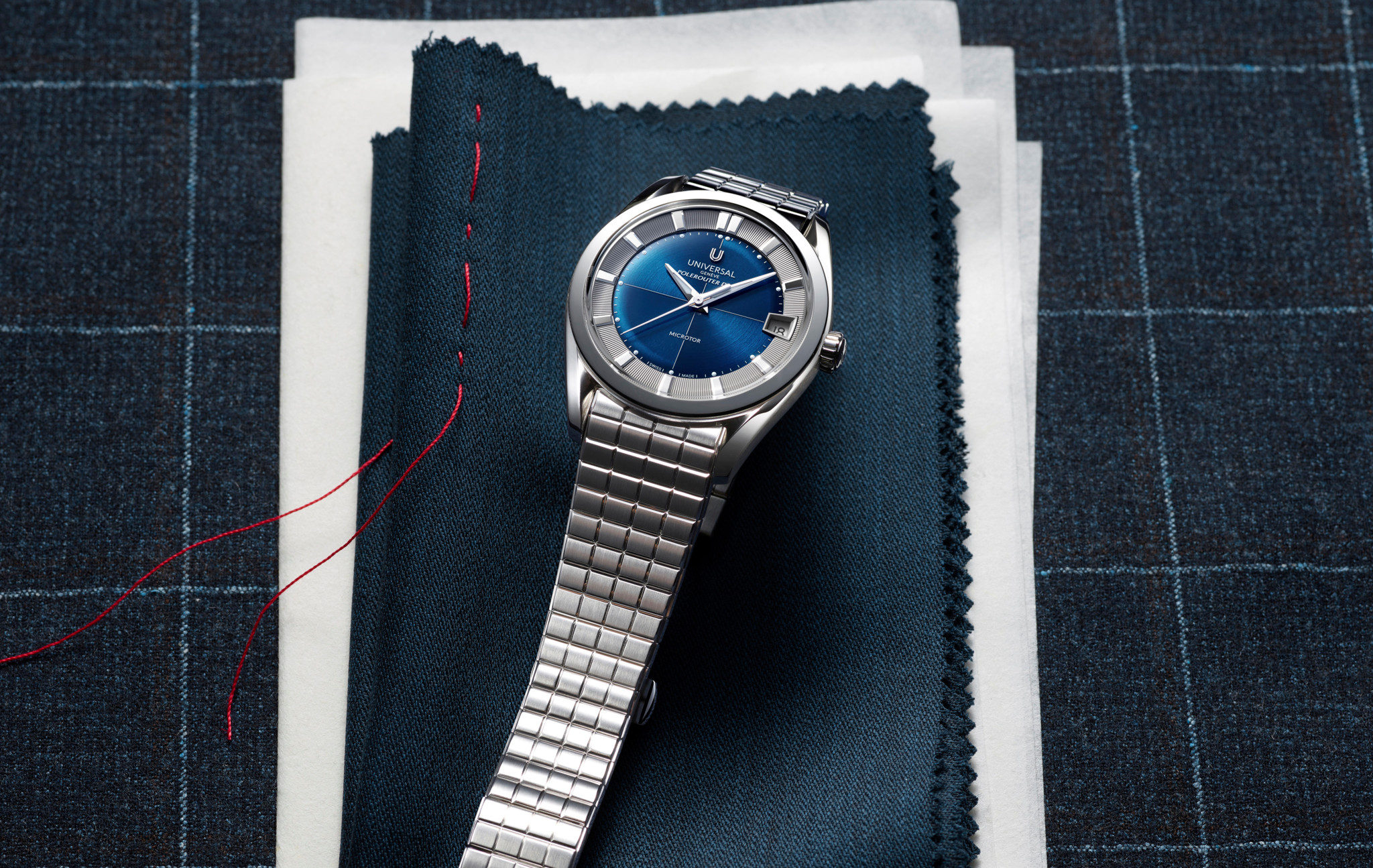 Montre élégante avec cadran bleu et bracelet en acier argenté, posée sur des échantillons de tissu bleu à carreaux avec un fil rouge
