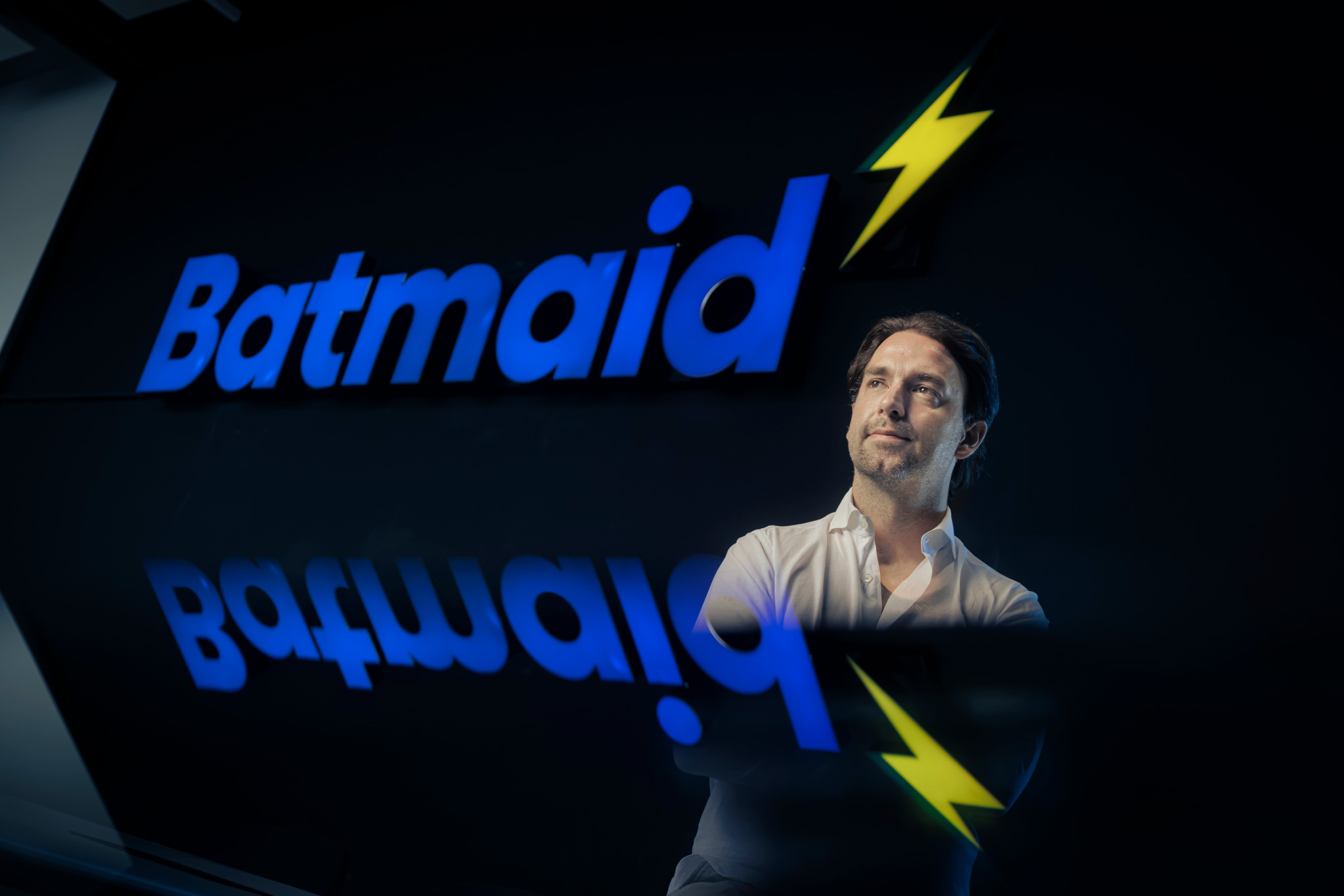 Andreas Schollin-Borg, CEO de Batmaid (Batgroup SA), devant le logo lumineux bleu et jaune de Batmaid, dans les bureaux de Lausanne.