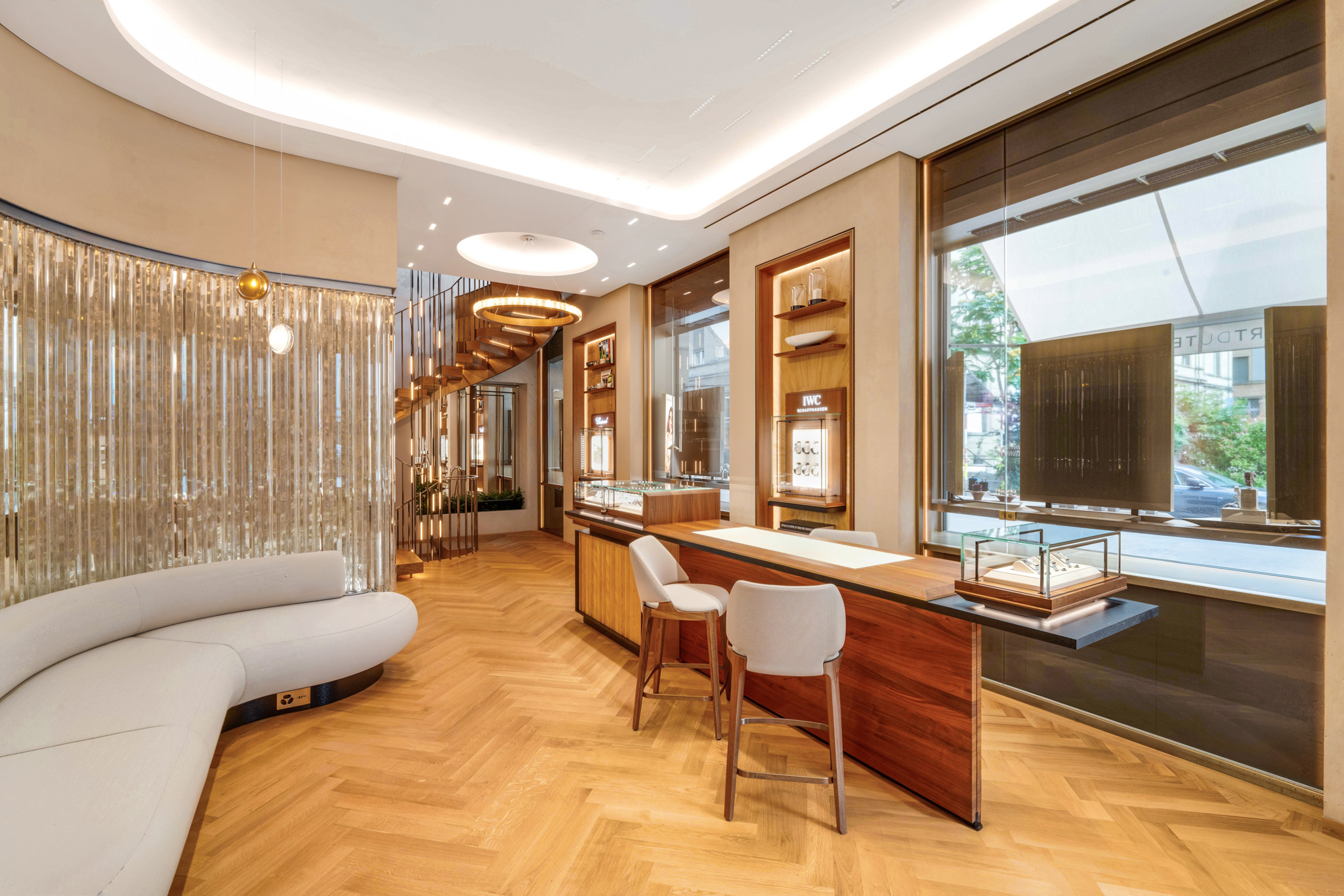 Intérieur élégant d’une bijouterie avec des vitrines en verre, des fauteuils modernes et un sol en bois clair, éclairé par une lumière tamisée.