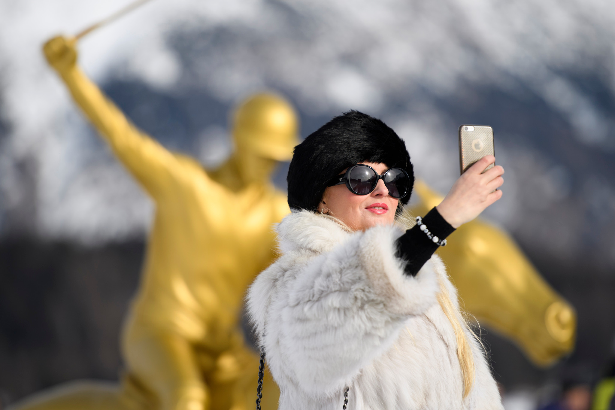 Une visiteuse en manteau de fourrure prend un selfie devant une statue dorée lors de la Snow Polo World Cup à St-Moritz.