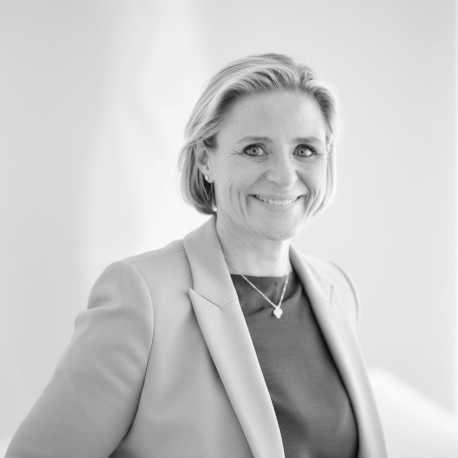 Portrait en noir et blanc d’une femme souriante en veste claire, portant un collier délicat, sur fond clair.