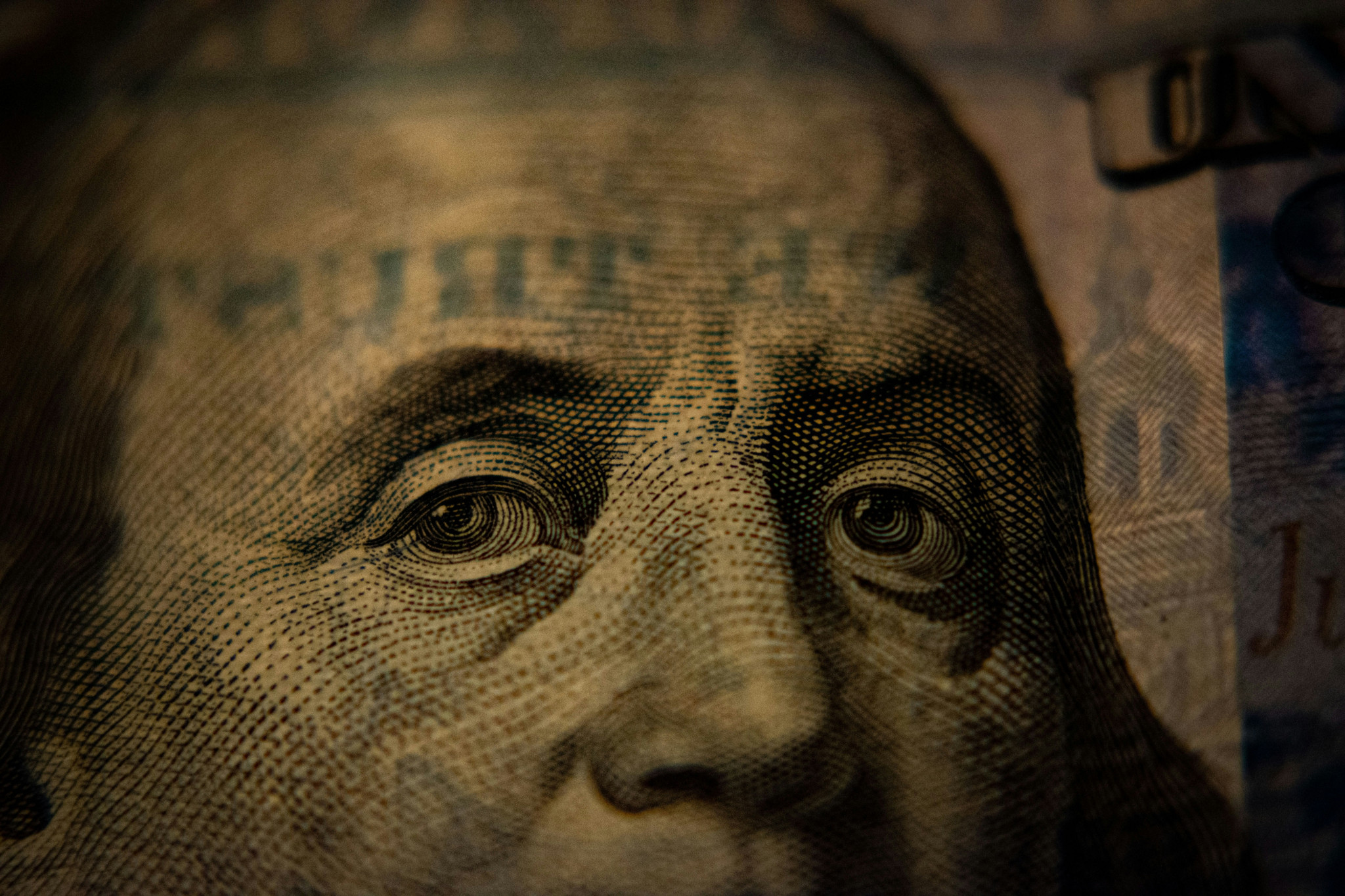 Gros plan sur le visage de Benjamin Franklin imprimé sur un billet de 100 dollars américains, éclairage sombre et dramatique.